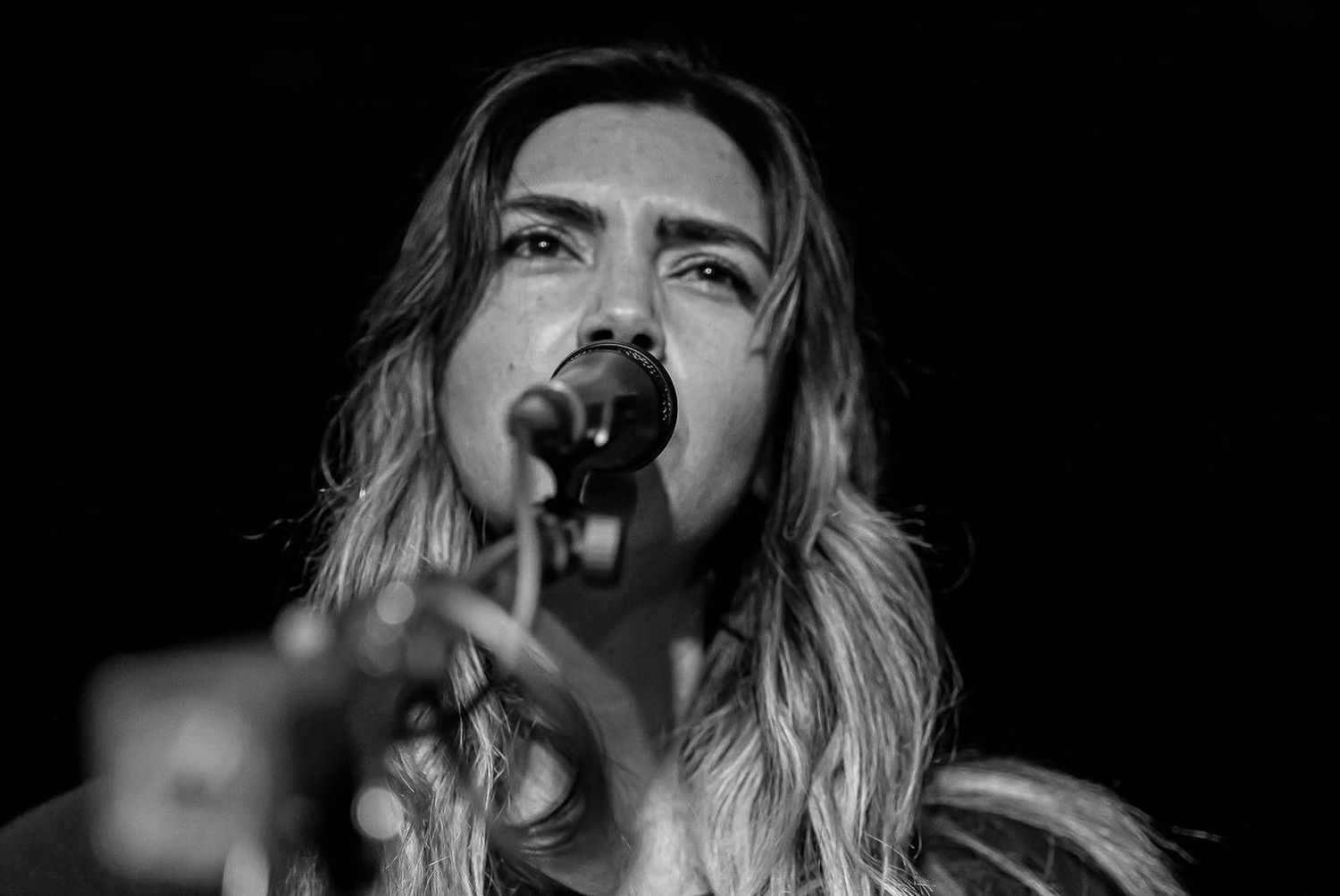 Singer performing on stage with microphone in dramatic black and white lighting.