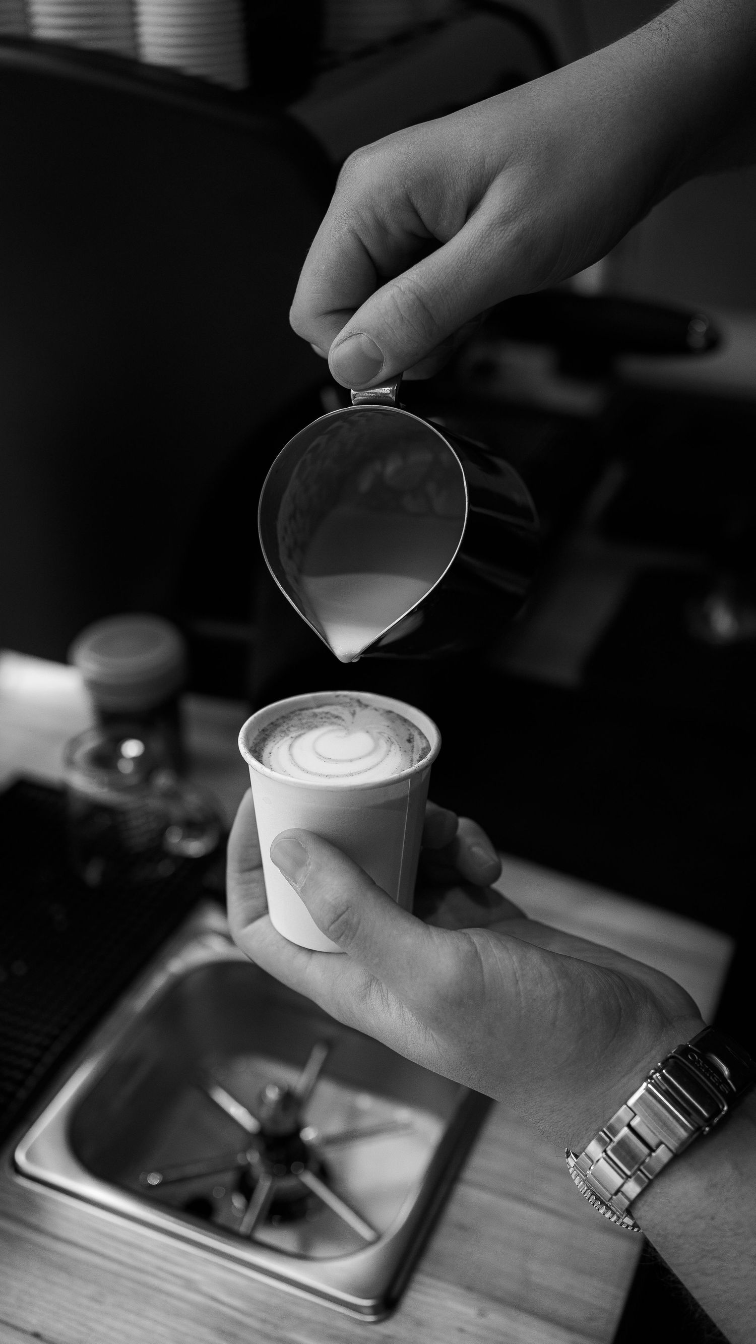 A barista creates latte art by pouring steamed milk into coffee in a sequence of black and white images.