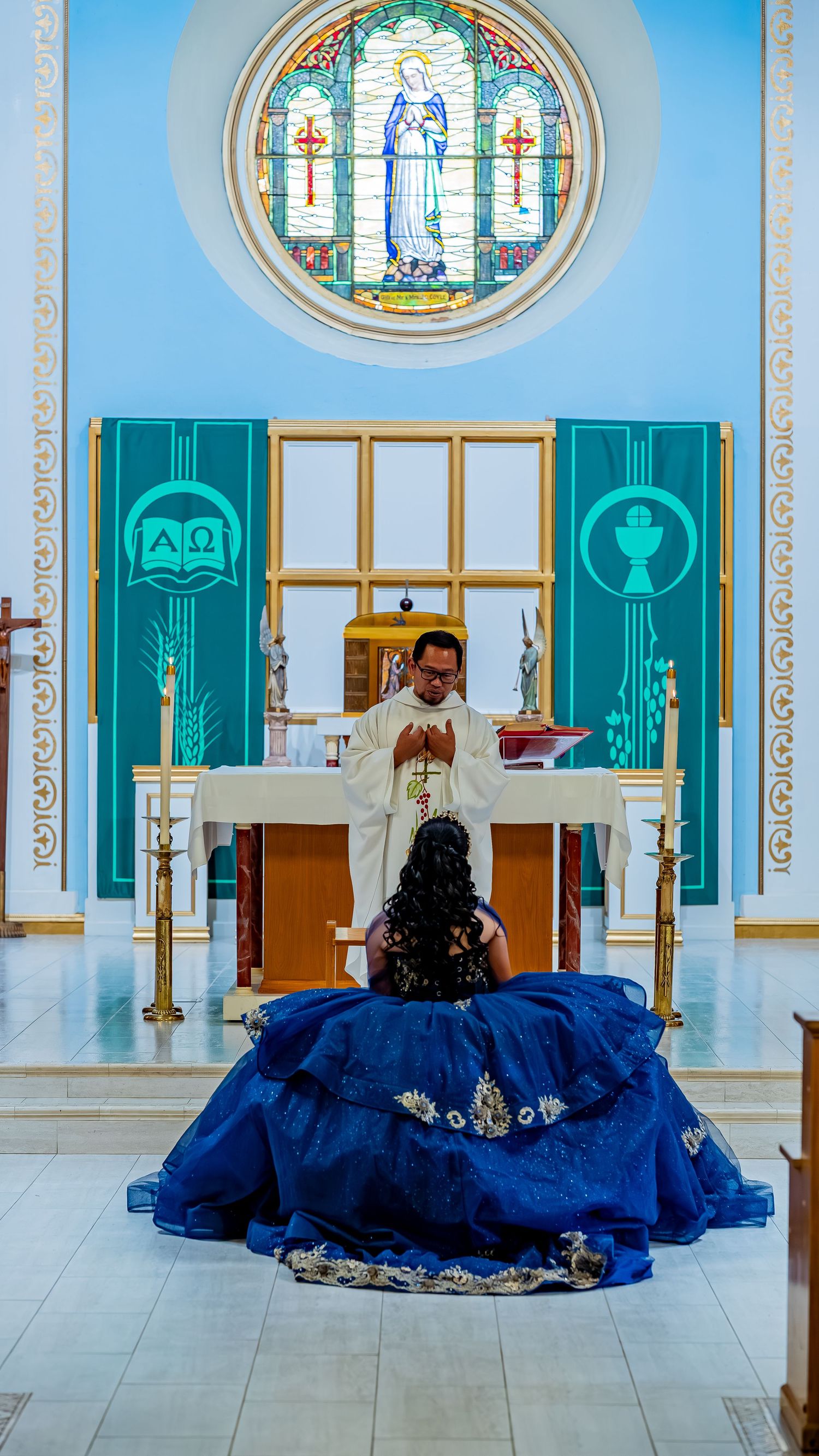 A navy blue ball gown spreads across a church floor with turquoise and gold religious decor.