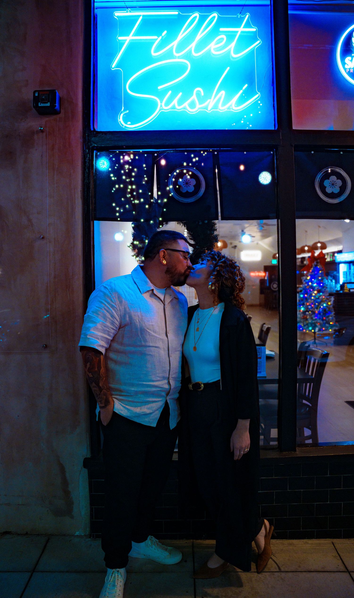 Nighttime portrait under blue neon Fillet Sushi sign with ambient lighting.