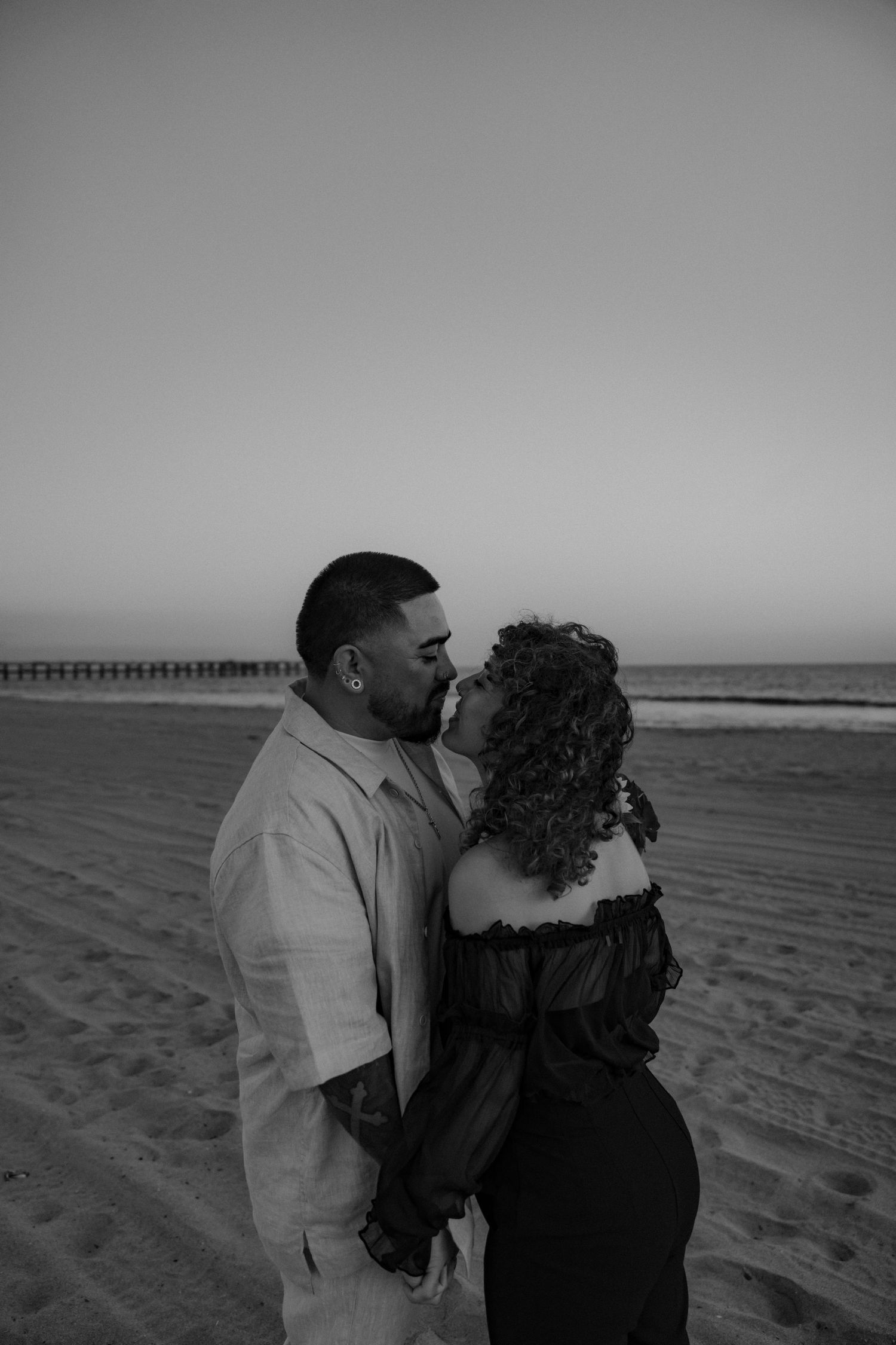 A romantic couple embraces on a serene beach at sunset, captured in a series of black and white photographs.