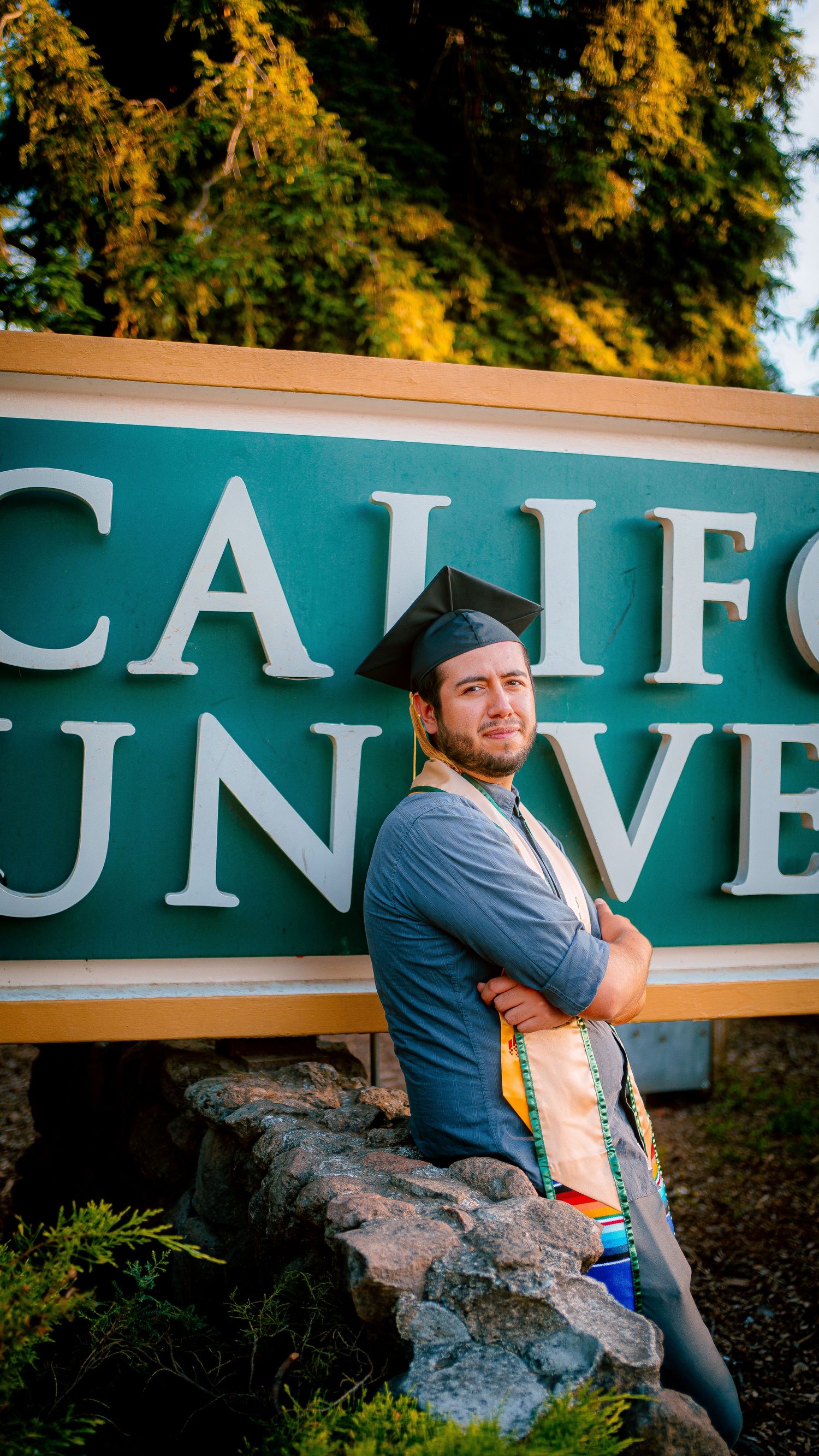 Graduate in casual attire posing by California State University signage.