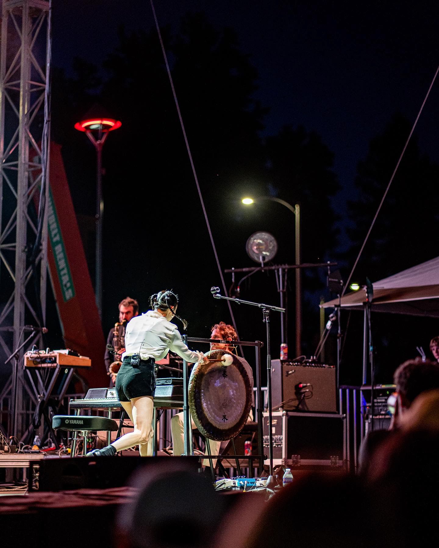 Wide shot of outdoor concert stage setup with lighting rigs and equipment at night.