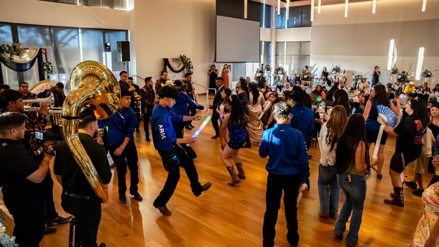 Large dance hall with hardwood floors and mirrors showing various dance couples in practice.