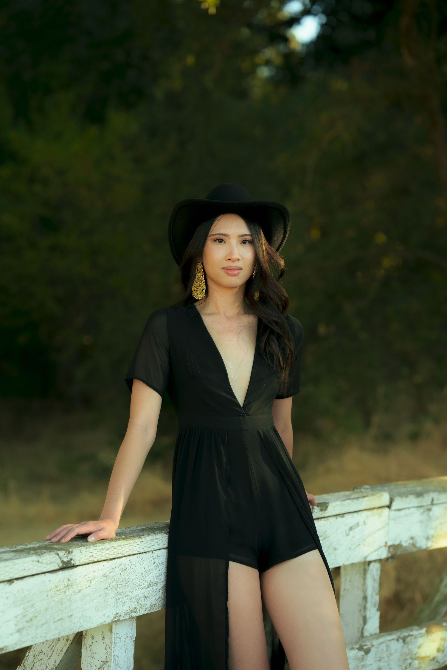 A stylish portrait on a white fence featuring a black romper dress and western hat.