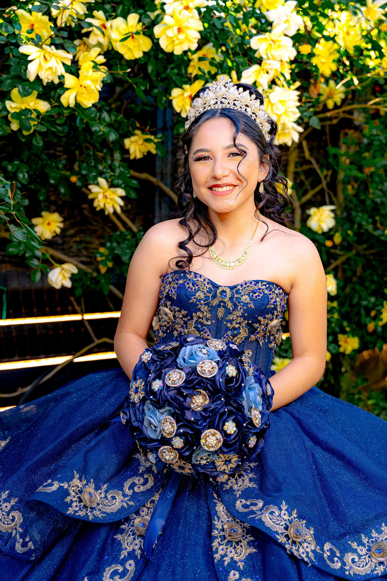A blue embellished ballgown photographed against yellow flowers in an outdoor setting.