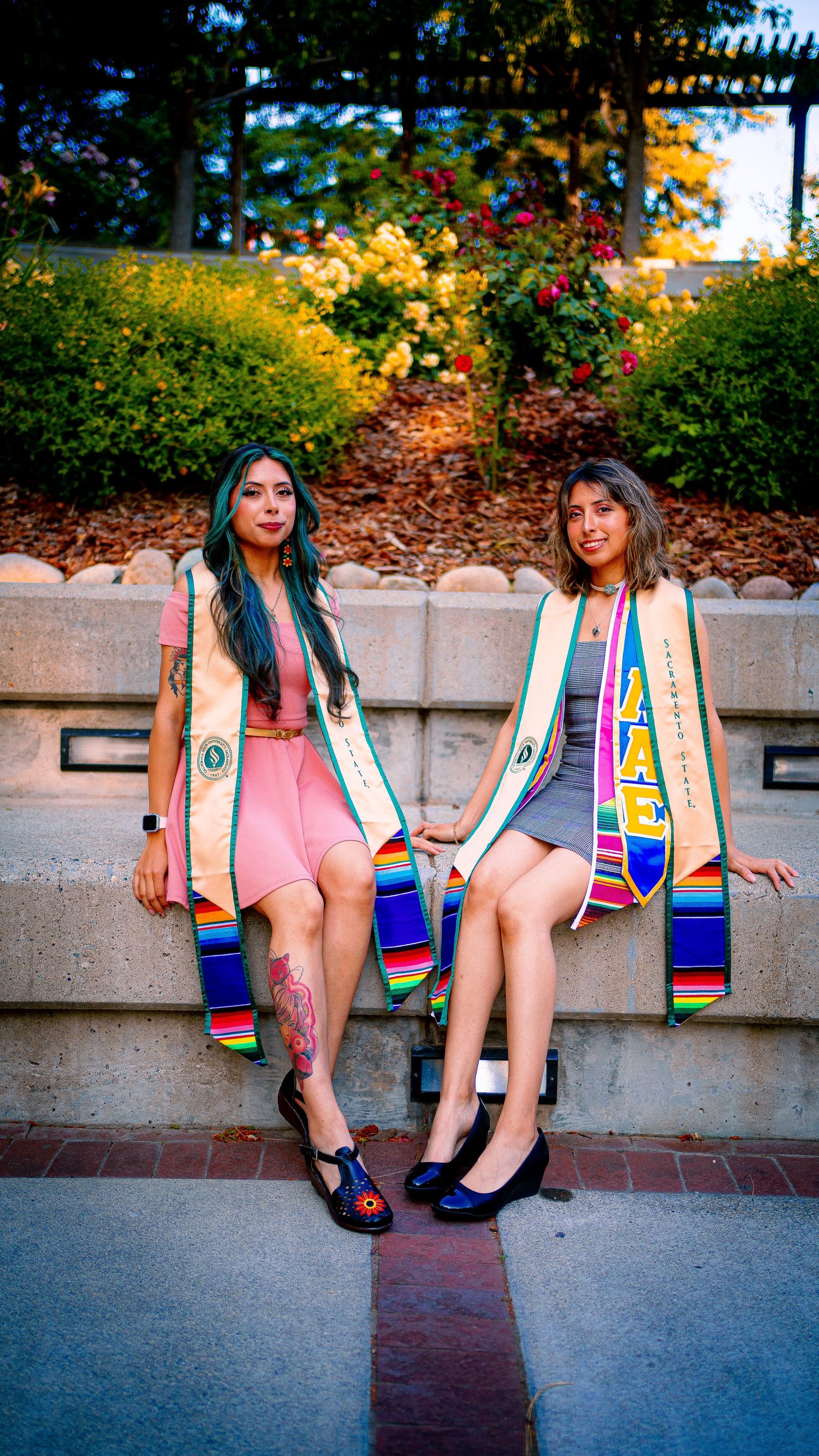 Graduates in colorful stoles sit on concrete steps during sunset photo session.