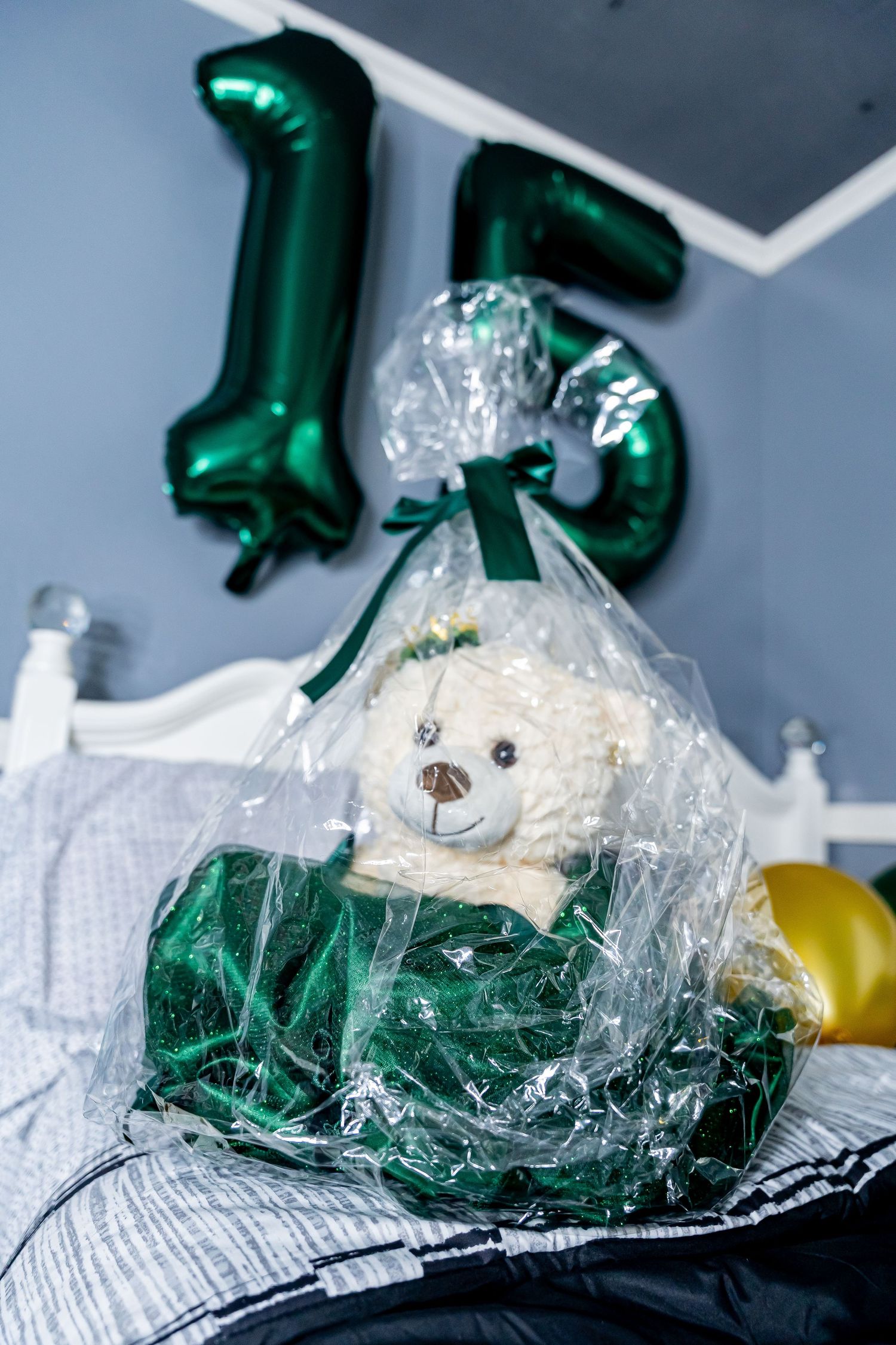 Green number 15 balloons with wrapped teddy bear gift against white furniture.