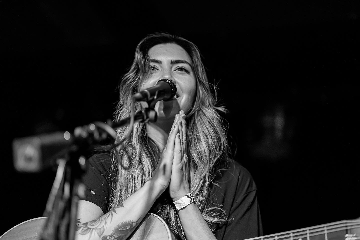 Black and white photo of a performer singing emotionally into a microphone with hands clasped together in prayer position.