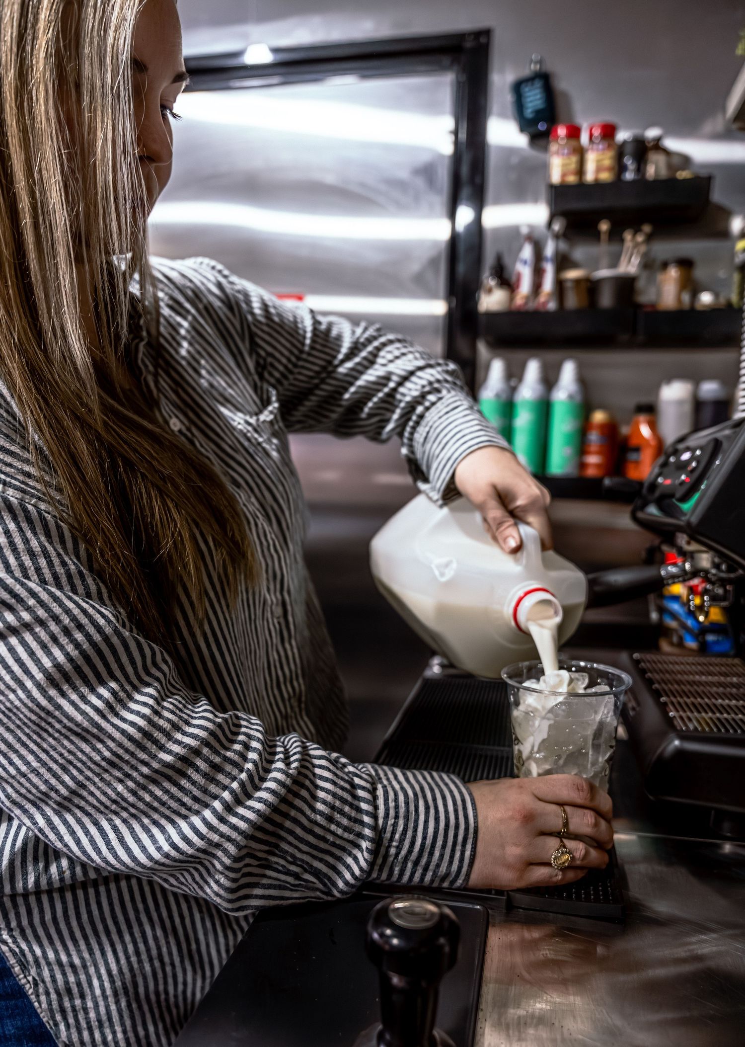 Barista in striped shirt preparing beverages behind coffee counter.