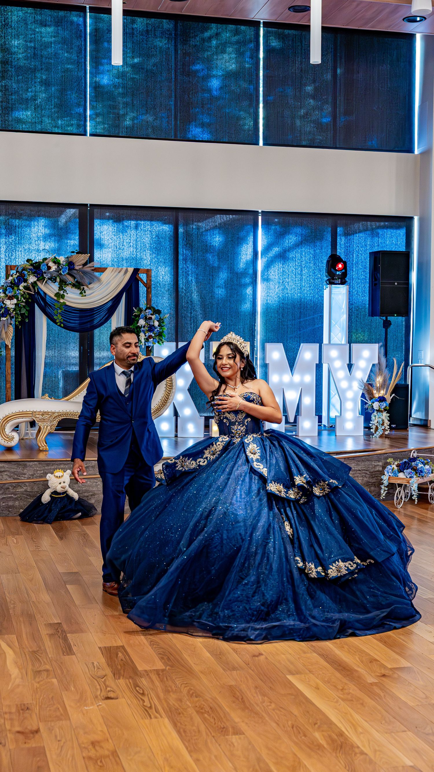 Dancers performing elegant spins and moves on a wooden dance floor in navy blue attire.