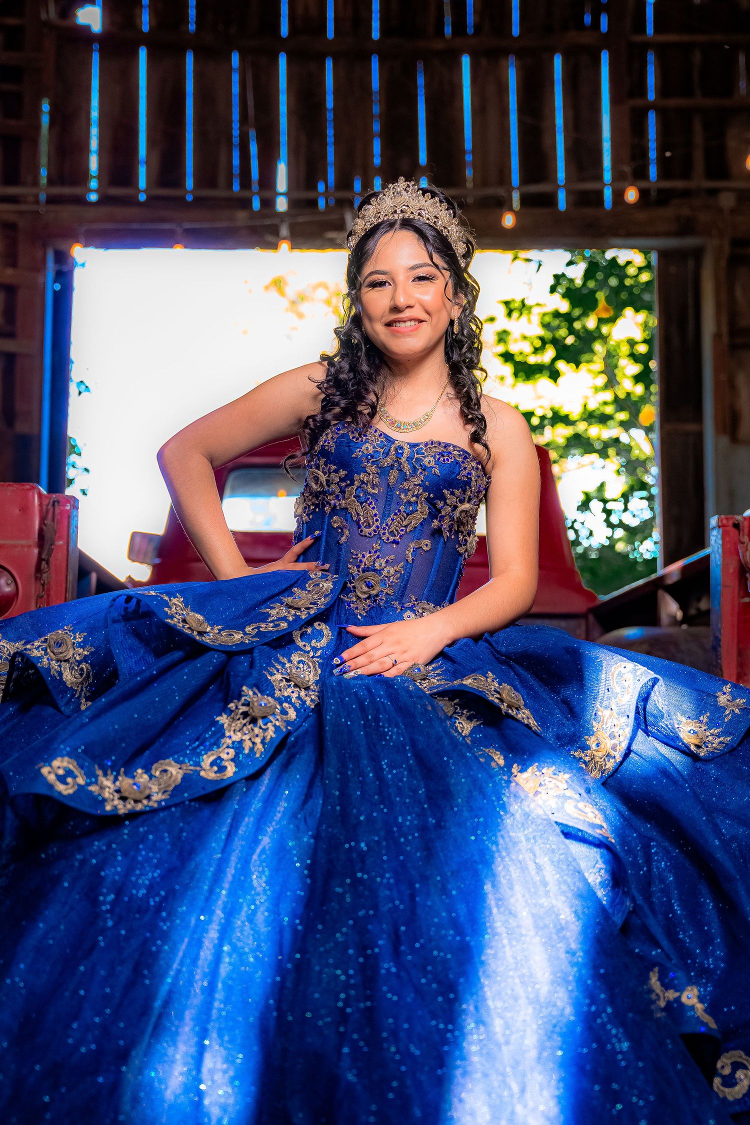 Stunning royal blue quinceañera dress with intricate gold embroidery photographed in rustic barn setting.