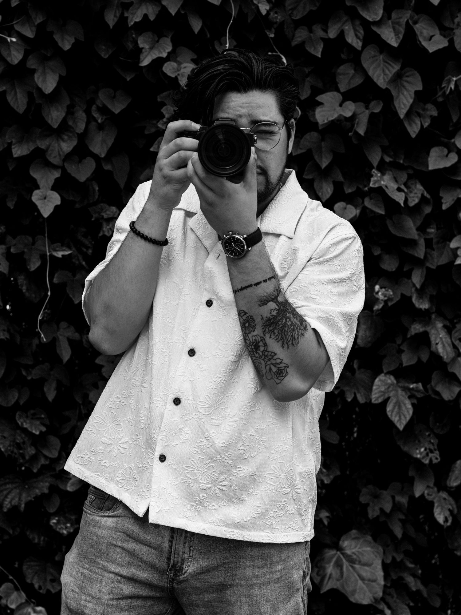 A series of black and white photos showing someone in a white button-up shirt against a leafy background.