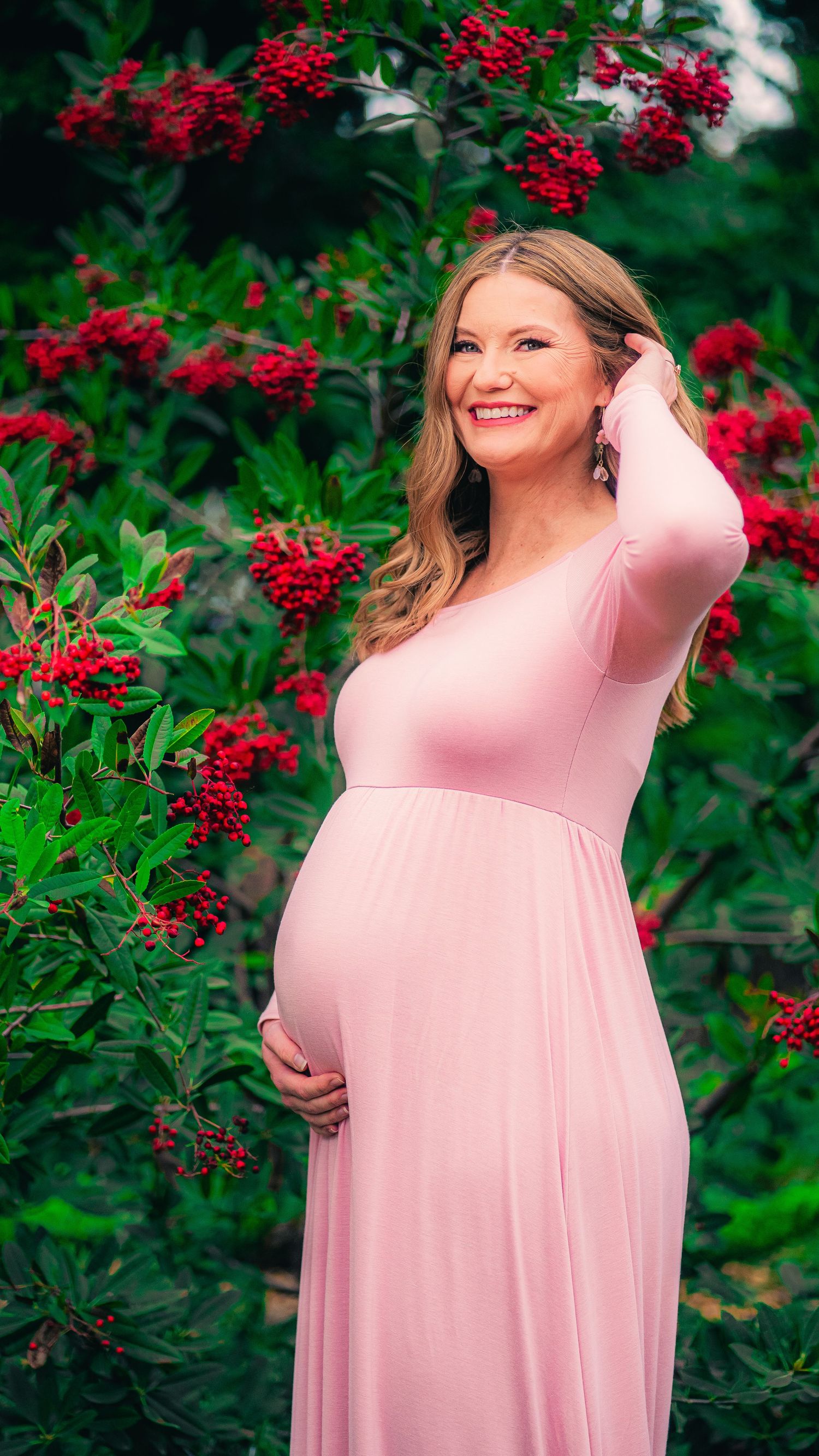 Person in flowing pink dress poses against vibrant red flowers and green foliage.
