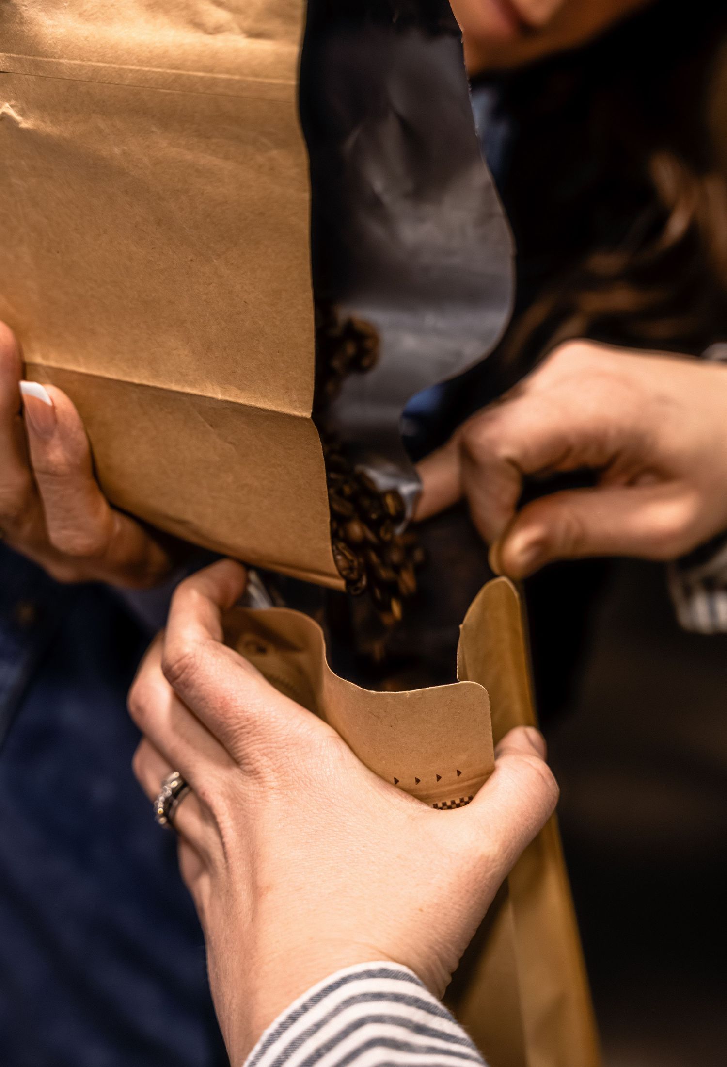 Hands pouring coffee beans into brown paper bag.