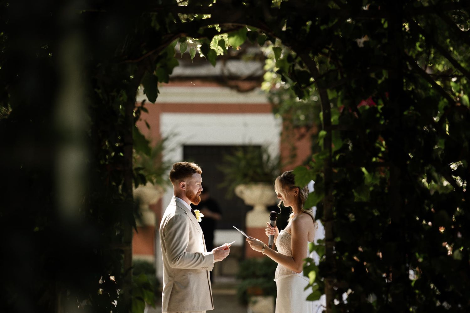 Emotional bride reading her wedding vows under the floral altar in the English gardens of Villa Delia during a ceremony in Spain.