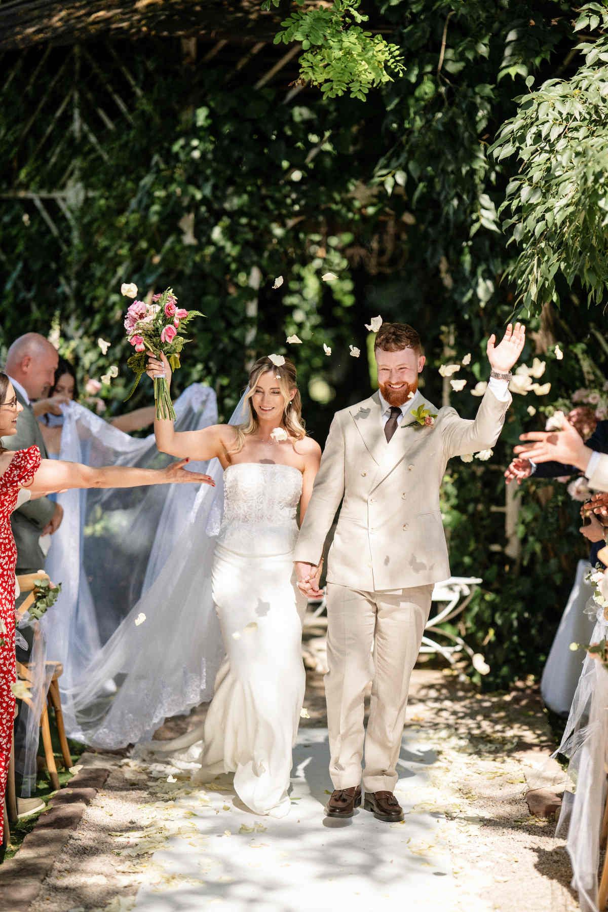 Just married bride and groom walking through a crowd of guests tossing petals. Joyful wedding exit at Villa Delia estate near Valencia.