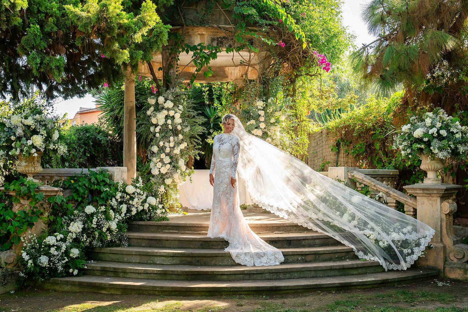 A complete bridal look featuring a long veil and a sophisticated hairstyle against a luxury floral ceremony arch.