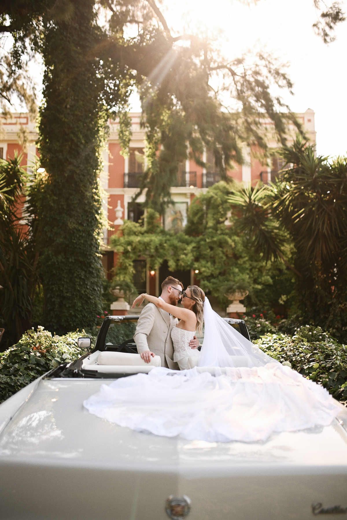 Wedding couple hugging inside a classic retro car against the historic Villa Delia estate facade. Romantic wedding photography in Spain