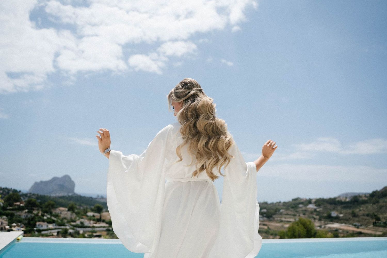 Bride in a robe with long wedding waves by the pool at Finca Marqués de Montemolar in Altea.