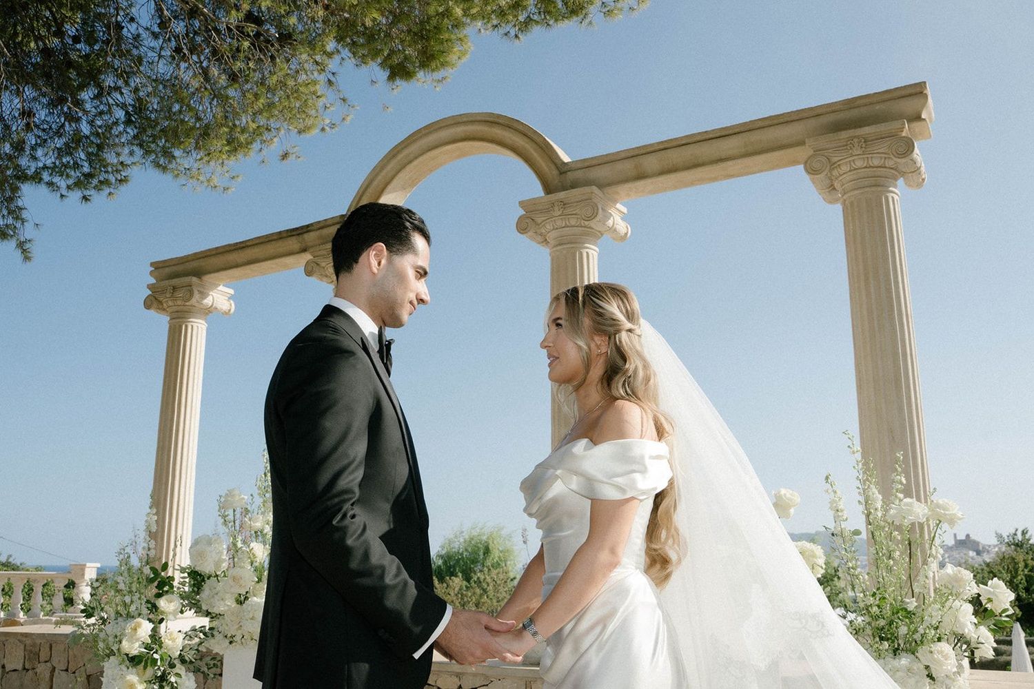 Groom holding bride's hands at the ceremony under the historic arch of Finca Marqués de Montemolar in Altea.