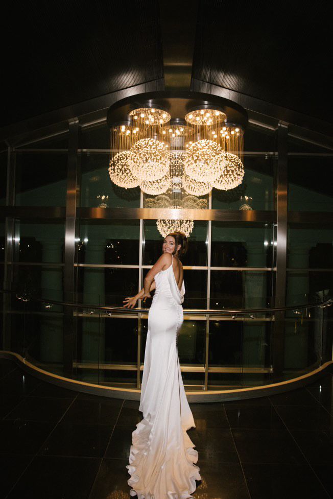A bride with a long dress train posing under grand chandeliers in the luxury lobby of Hotel Las Arenas