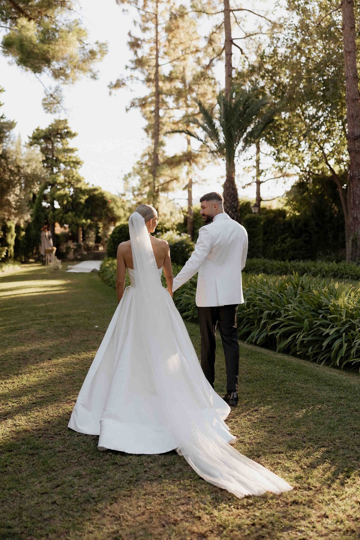 Romantic bride and groom walking through the dappled sunlight of the lush botanical gardens at the Casa Santonja estate in Spain.
