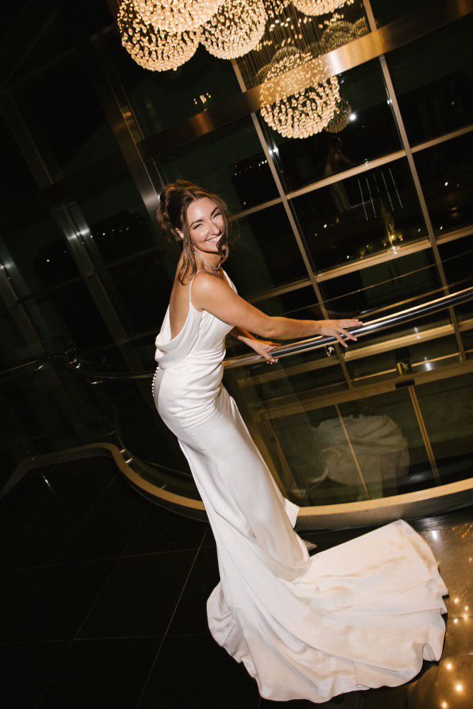 Wide-angle bridal portrait showcasing a long dress train, grand columns, and luxury chandeliers at Las Arenas Valencia