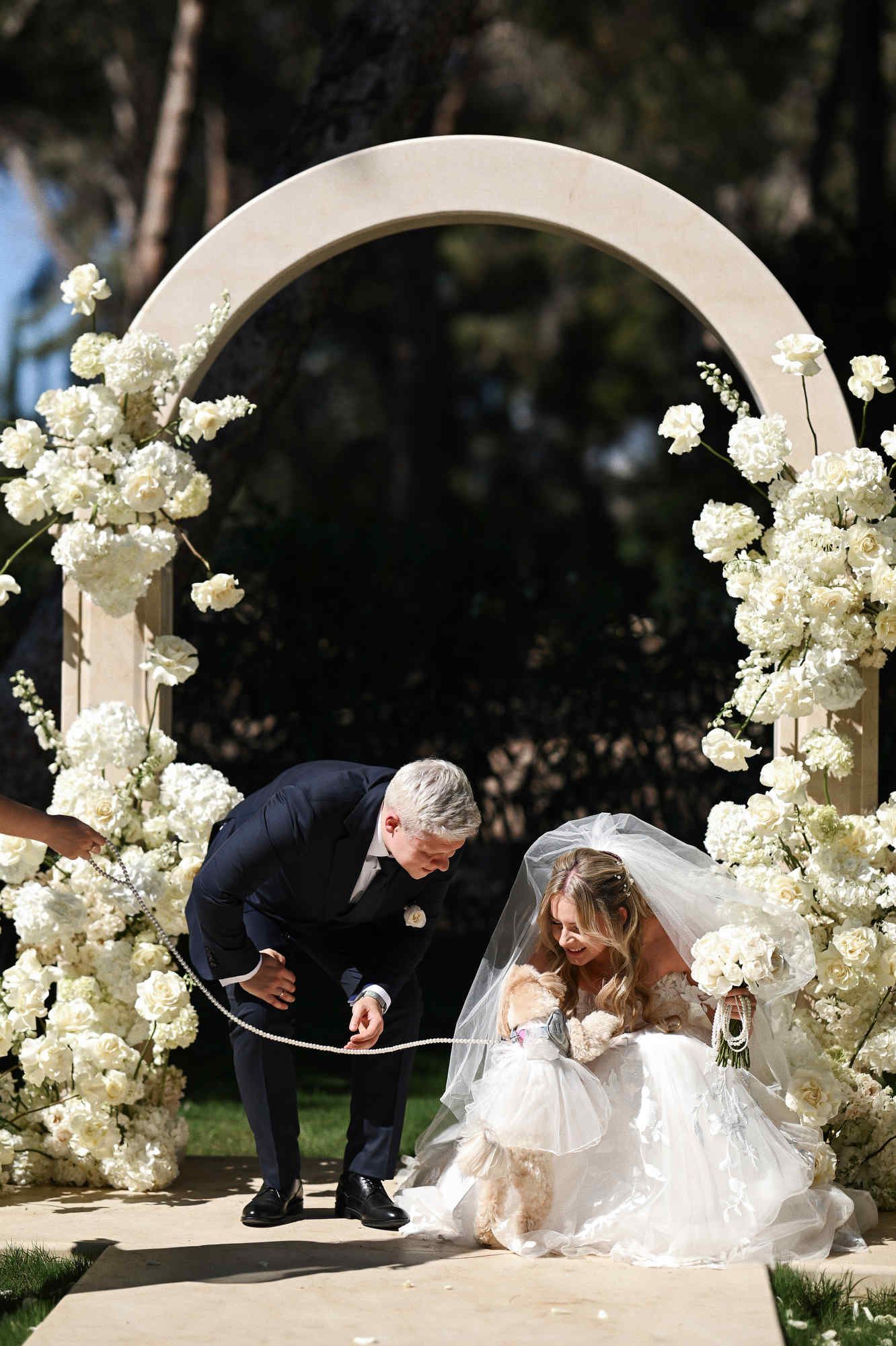 Happy bride and groom posing with their dog by the floral wedding arch during a ceremony at Finca El Senoret