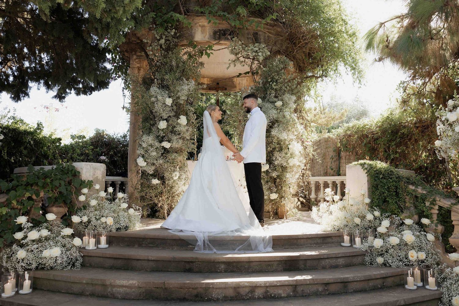 Elegant bride standing against the iconic stone walls and Mediterranean greenery of the Casa Santonja estate in Spain.