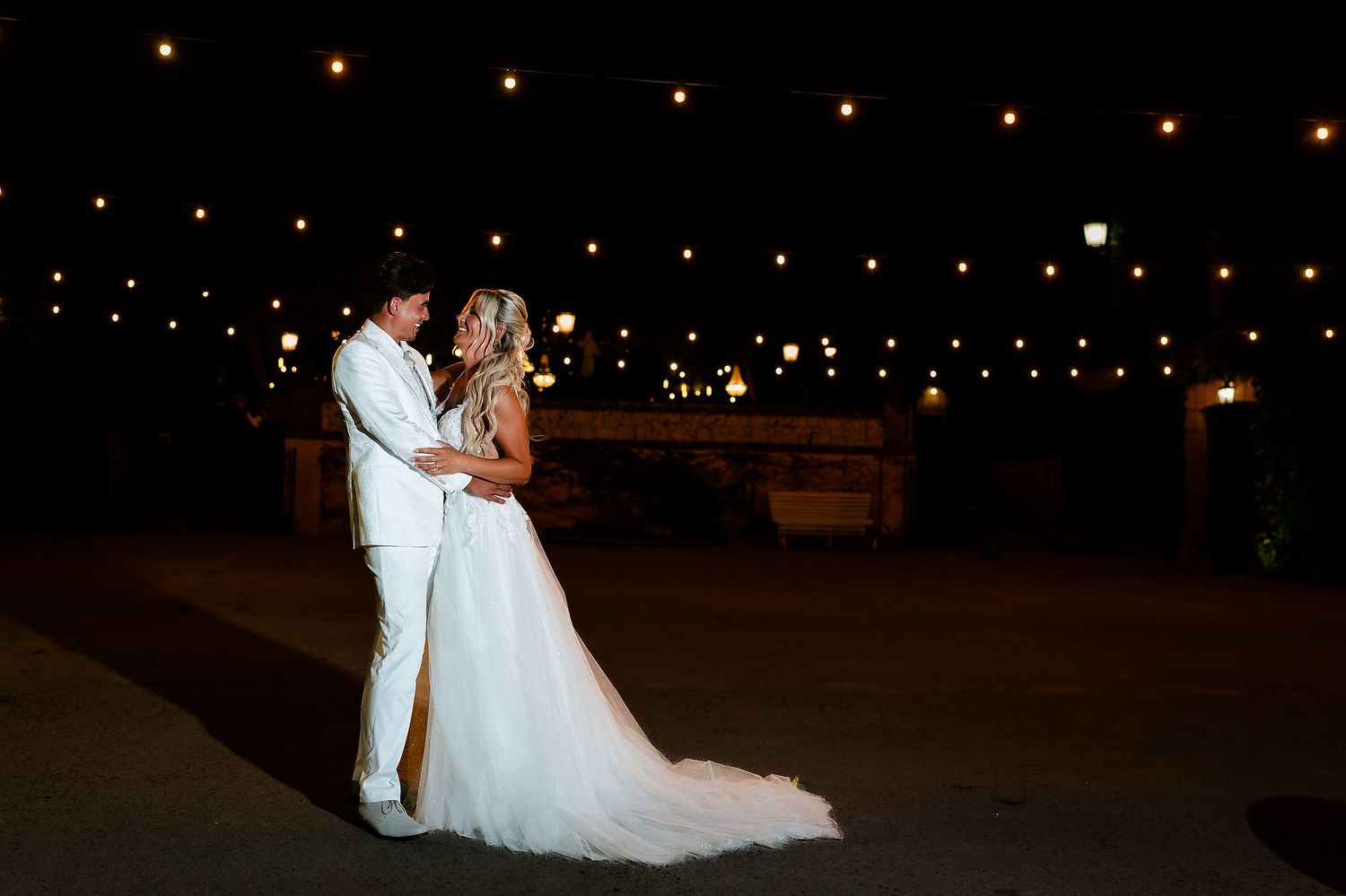 Atmospheric evening wedding portrait of the couple embracing against warm fairy lights in the gardens of Casa Santonja.