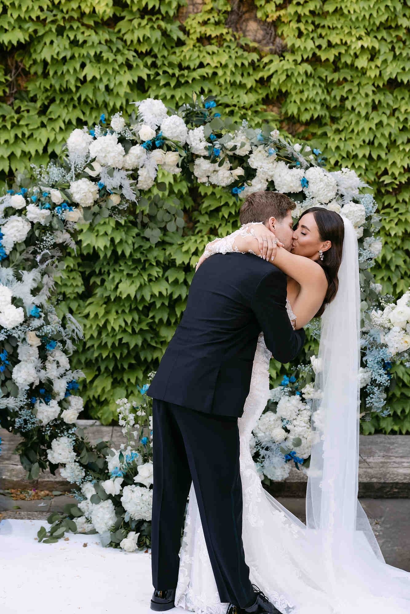 The newlyweds sharing a romantic kiss at their wedding ceremony arch with the majestic castle background