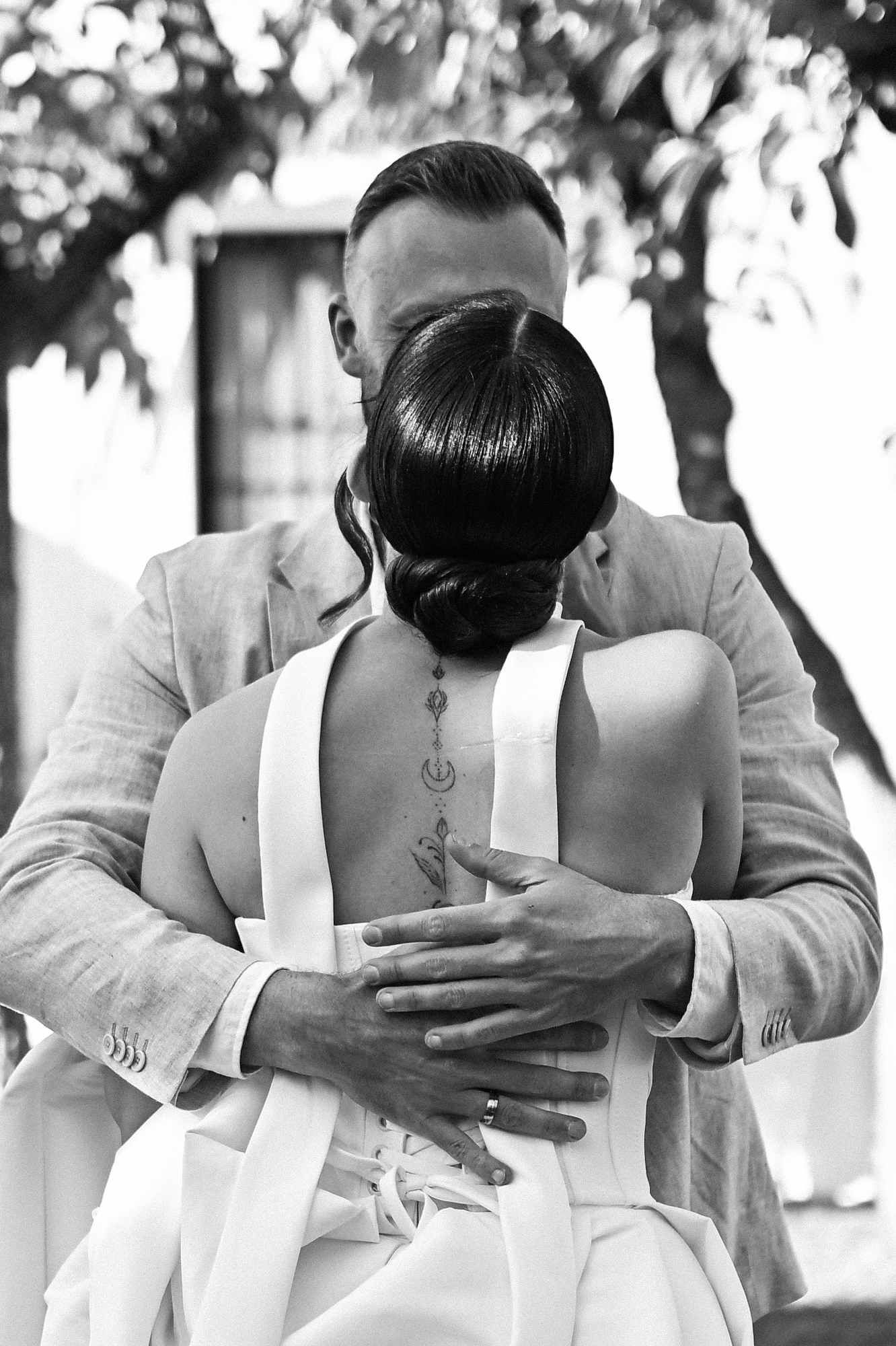 Atmospheric black and white photo of the groom hugging the bride tightly, showing the elegant details of her hairstyle from behind.
