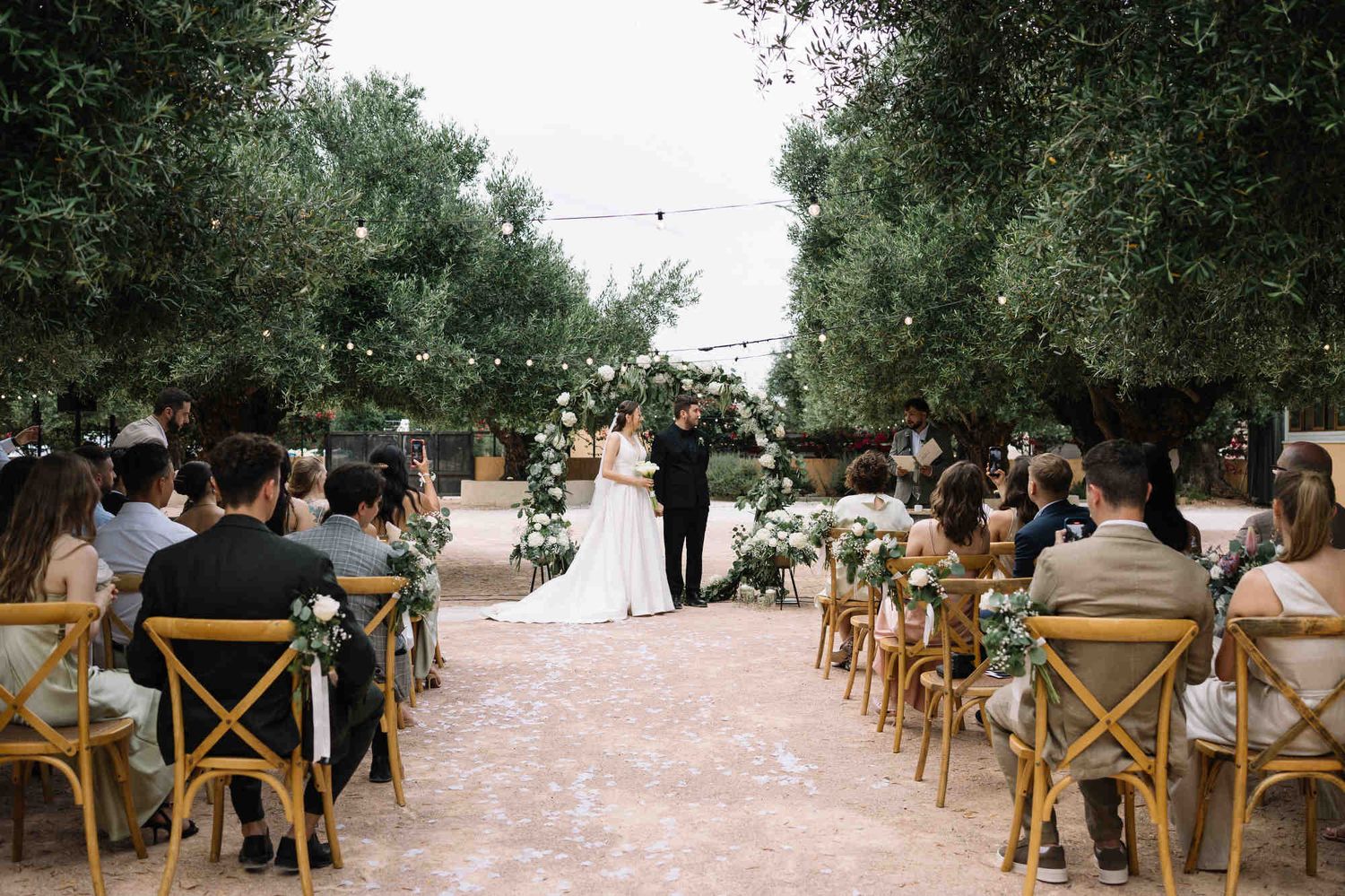 Wide shot of the wedding ceremony at Alqueria del Xúquer altar, with guests, groom, and bride in the heart of the Valencian countryside.