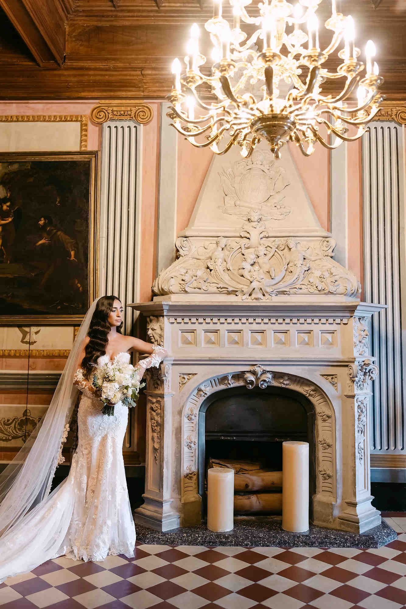 Full-length bridal portrait by the historic fireplace and grand chandelier, embodying a timeless and modern classic aesthetic
