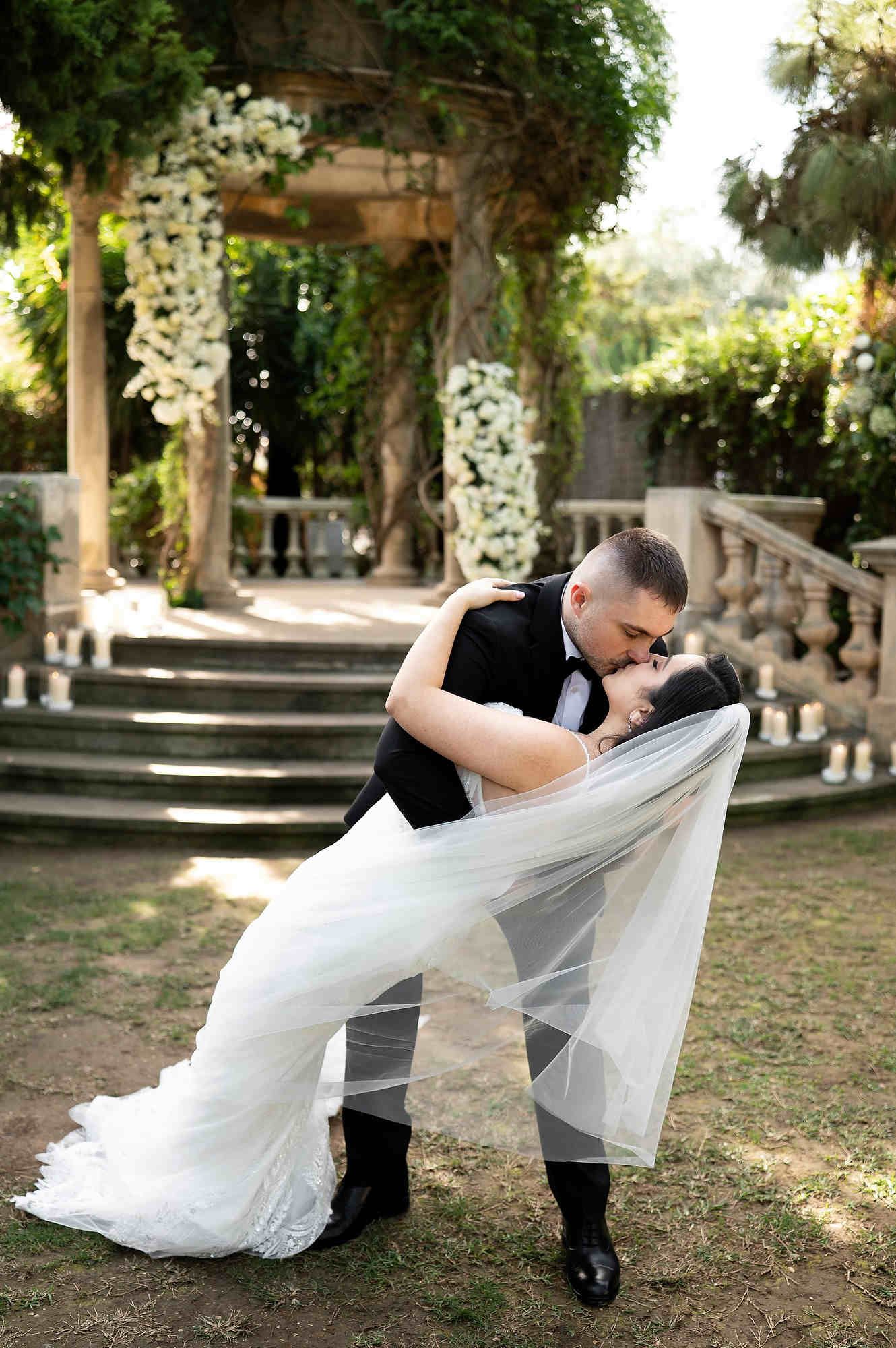 An editorial dip-kiss moment by the groom and bride in front of a luxury floral wedding arch.