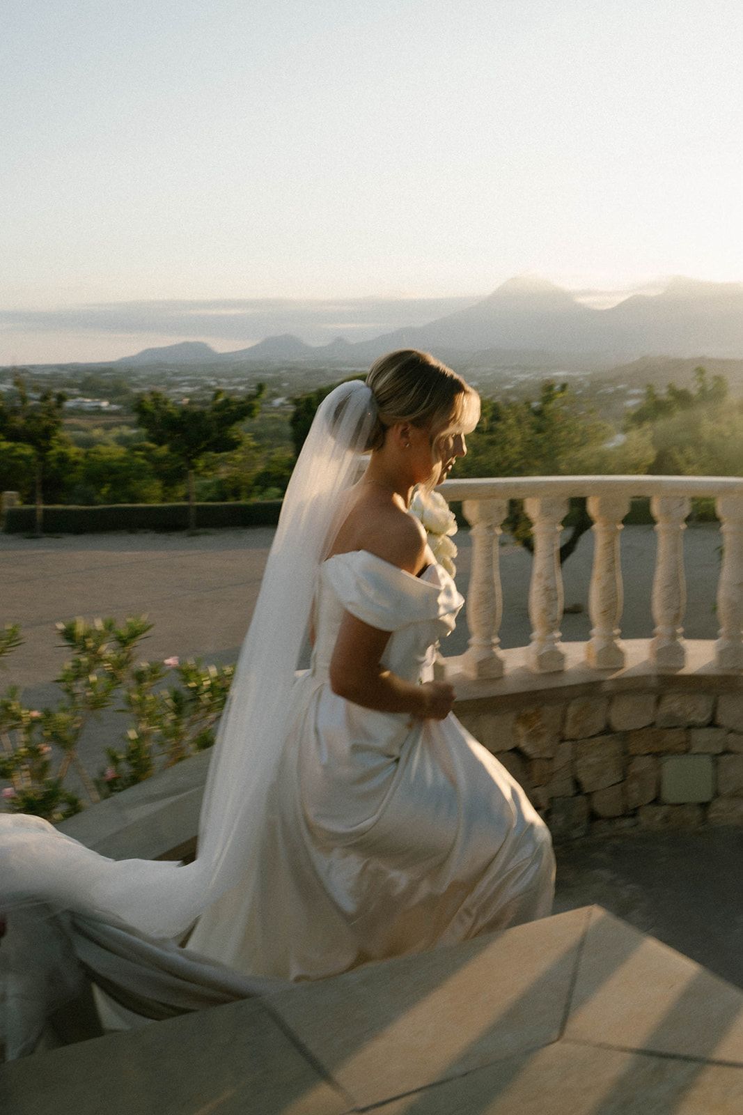Bride descending the stairs in golden sunset light at Finca Marqués de Montemolar with stunning makeup and hair by Anastasia Larionova.