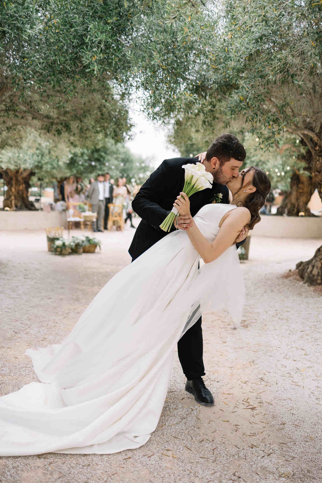 Romantic moment of a groom dipping and kissing his bride during their wedding photoshoot at the historic Alqueria del Xúquer in Spain.