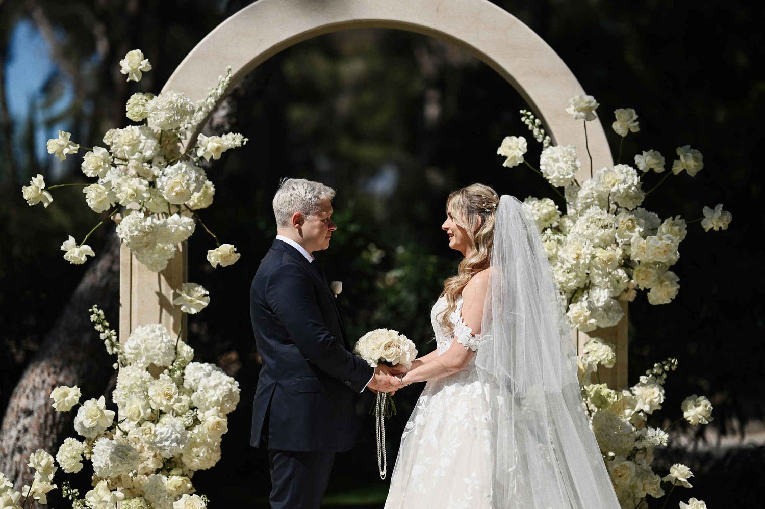 Bride and groom by the marble arch at Finca El Senoret on their wedding day in Valencia, Spain, showcasing flawless makeup and hair.