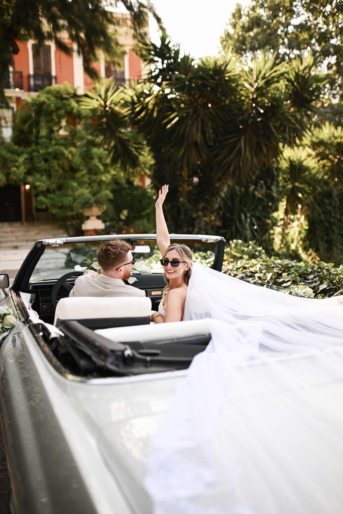 Bride waving from a vintage car. Perfect long-lasting wedding makeup and hair design staying pristine throughout the entire celebration day.