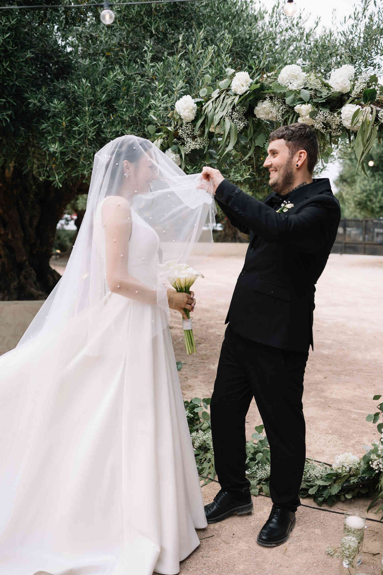 Groom lifting the bridal veil for the first look during the ceremony at Alqueria del Xúquer, showing radiant bridal makeup.
