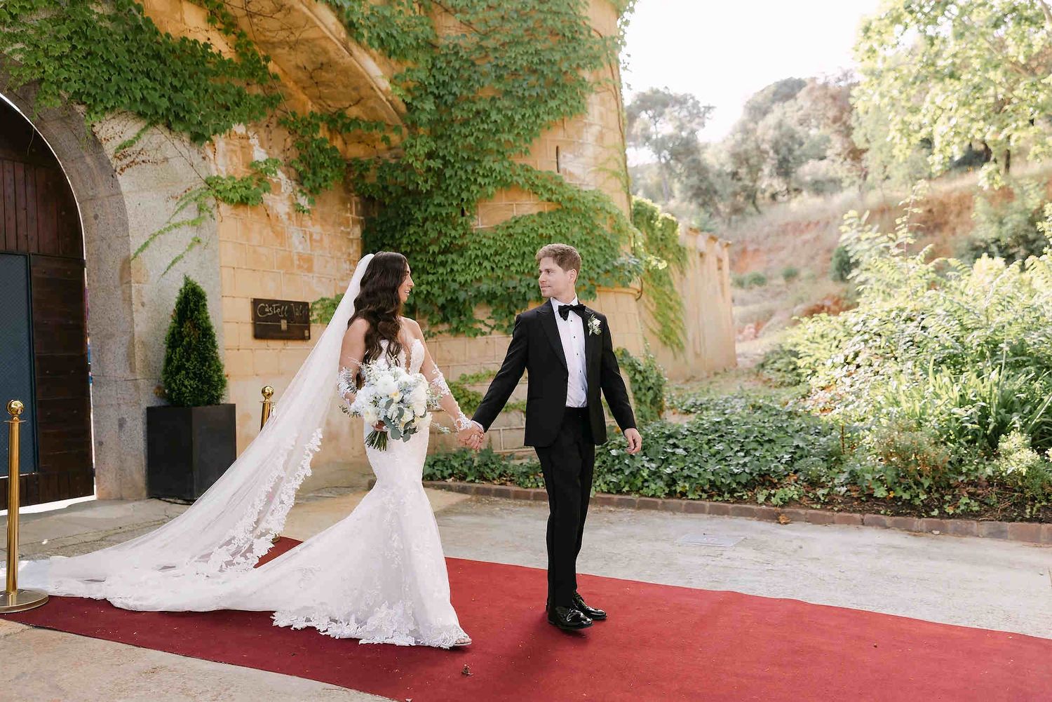Bride and groom walking on the red carpet at Castell Jalpí in Barcelona, featuring a professional and long-lasting bridal hair and makeup