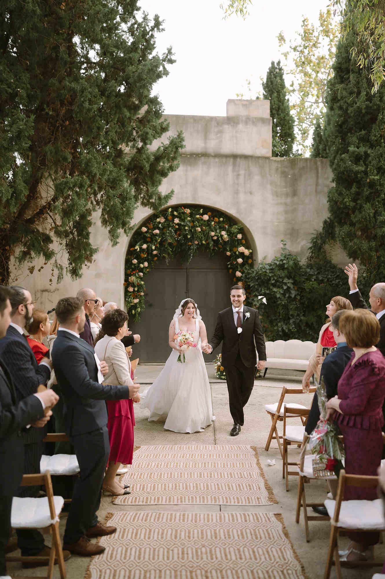 Newlyweds walking through a corridor of cheering guests after their wedding ceremony at Mas d’Alzedo