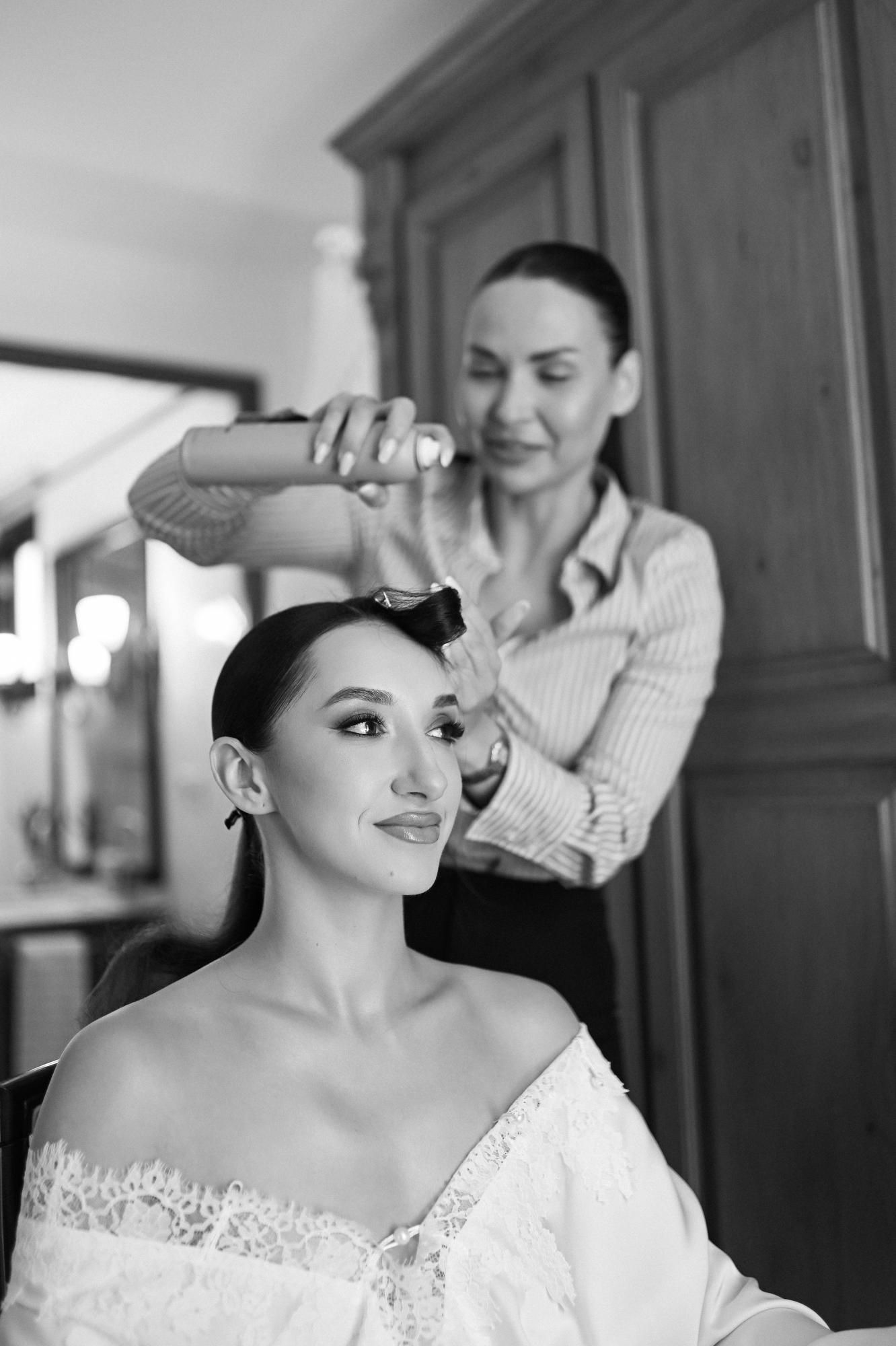 Hairstylist Anastasia Larionova creating bridal look at Villa Paula Valencia as bride holds hairspray bottle during preparation.