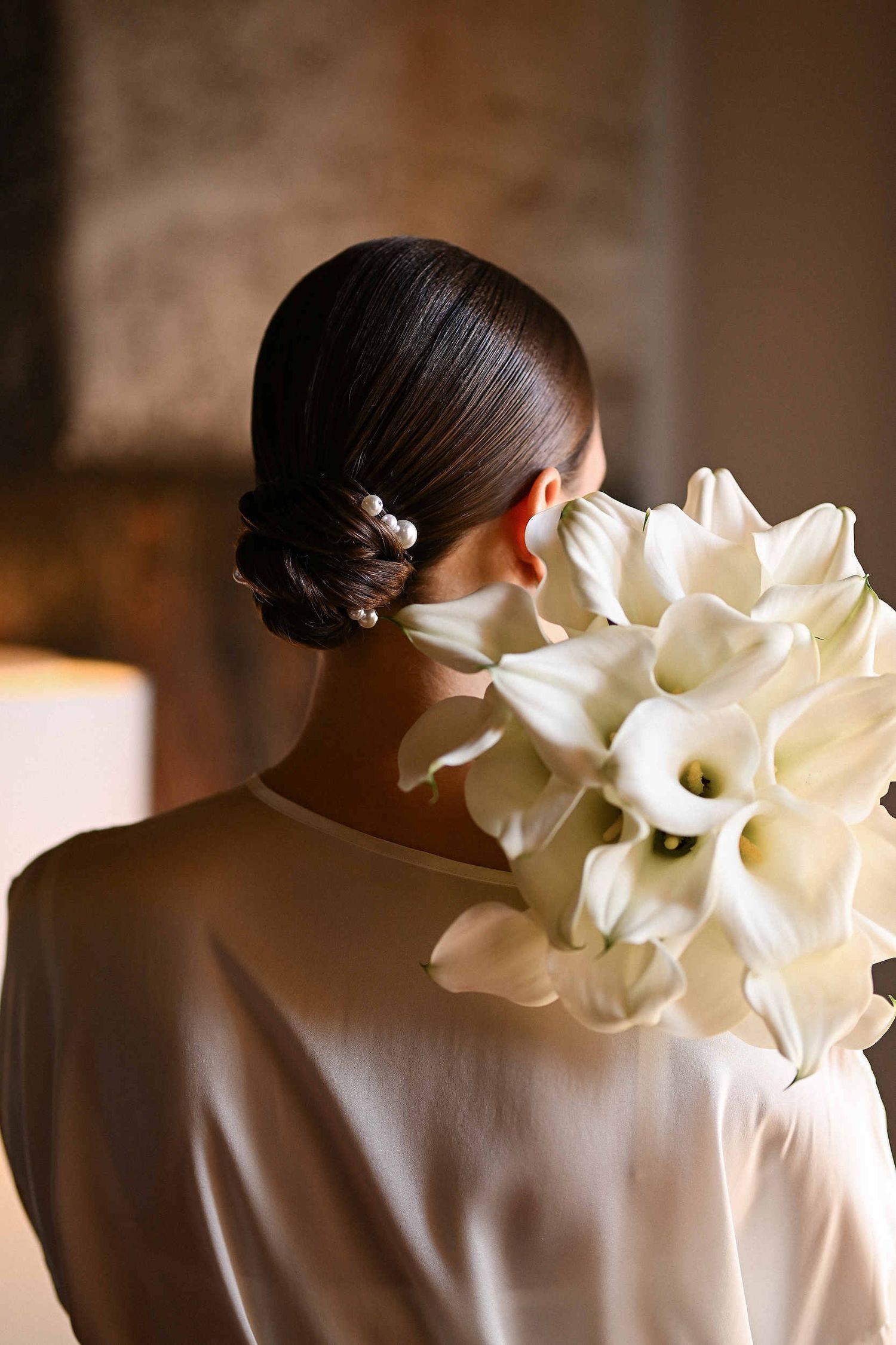 Bridal low bun with calla lilies in a Valencia hotel room. Professional makeup and hair at La Cartoixa d'Ara Christi