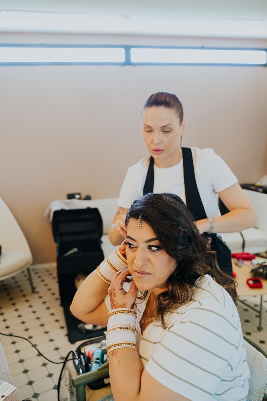 A candid moment of the makeup artist applying bridal makeup and styling hair for one of the brides in traditional attire.