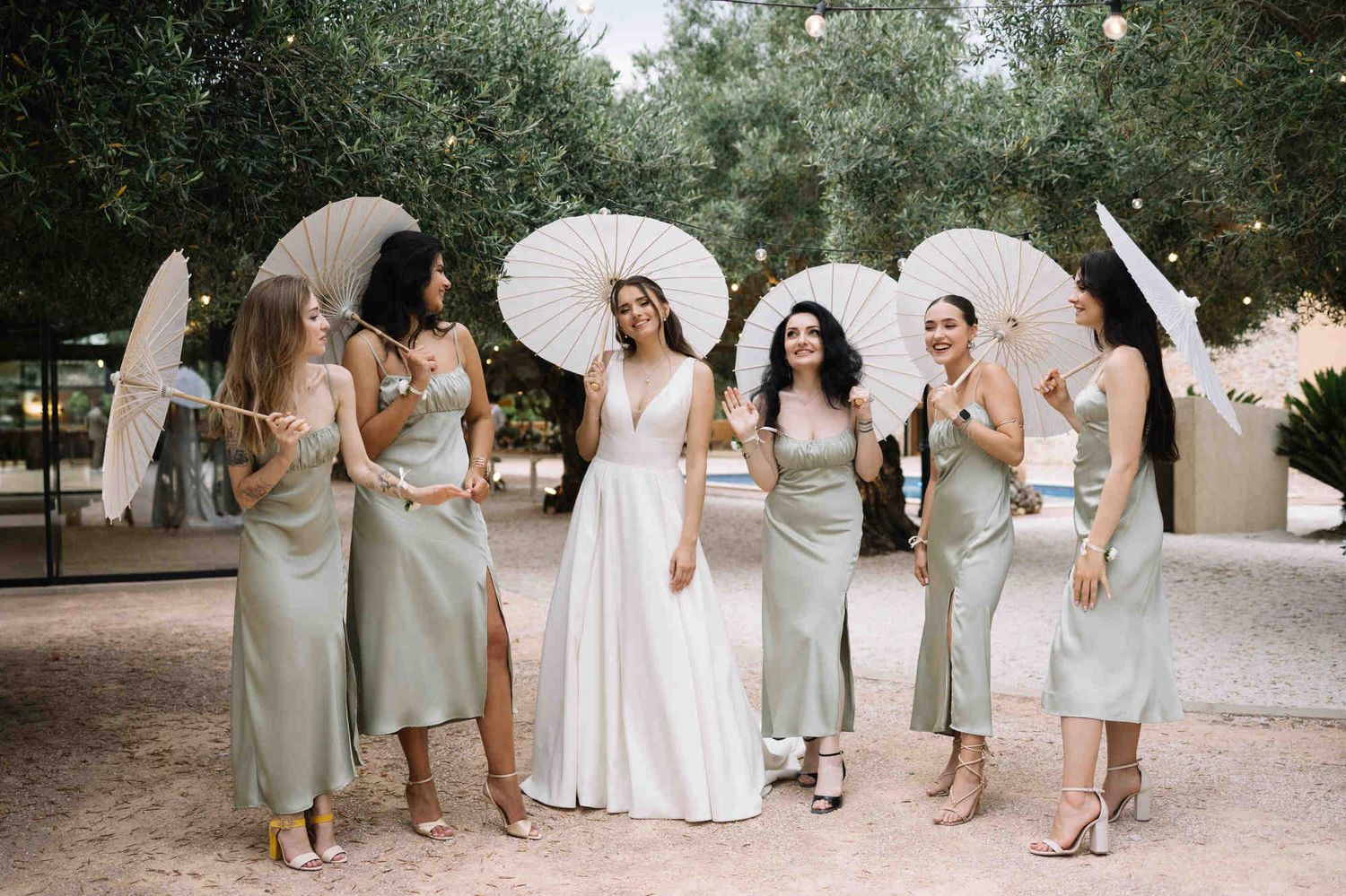 Bride and bridesmaids with stylish sun umbrellas during a garden ceremony at Alqueria del Xúquer, showcasing perfect group beauty looks.