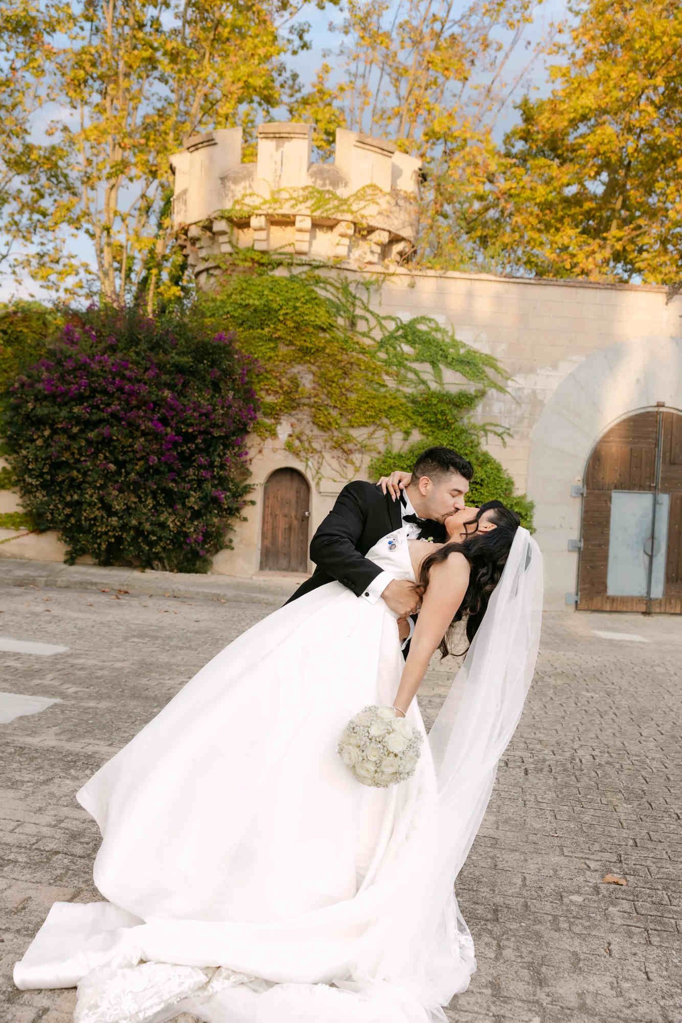 The groom dipping and kissing the bride in the courtyard of Castell Jalpí, capturing an elegant and cinematic wedding moment.