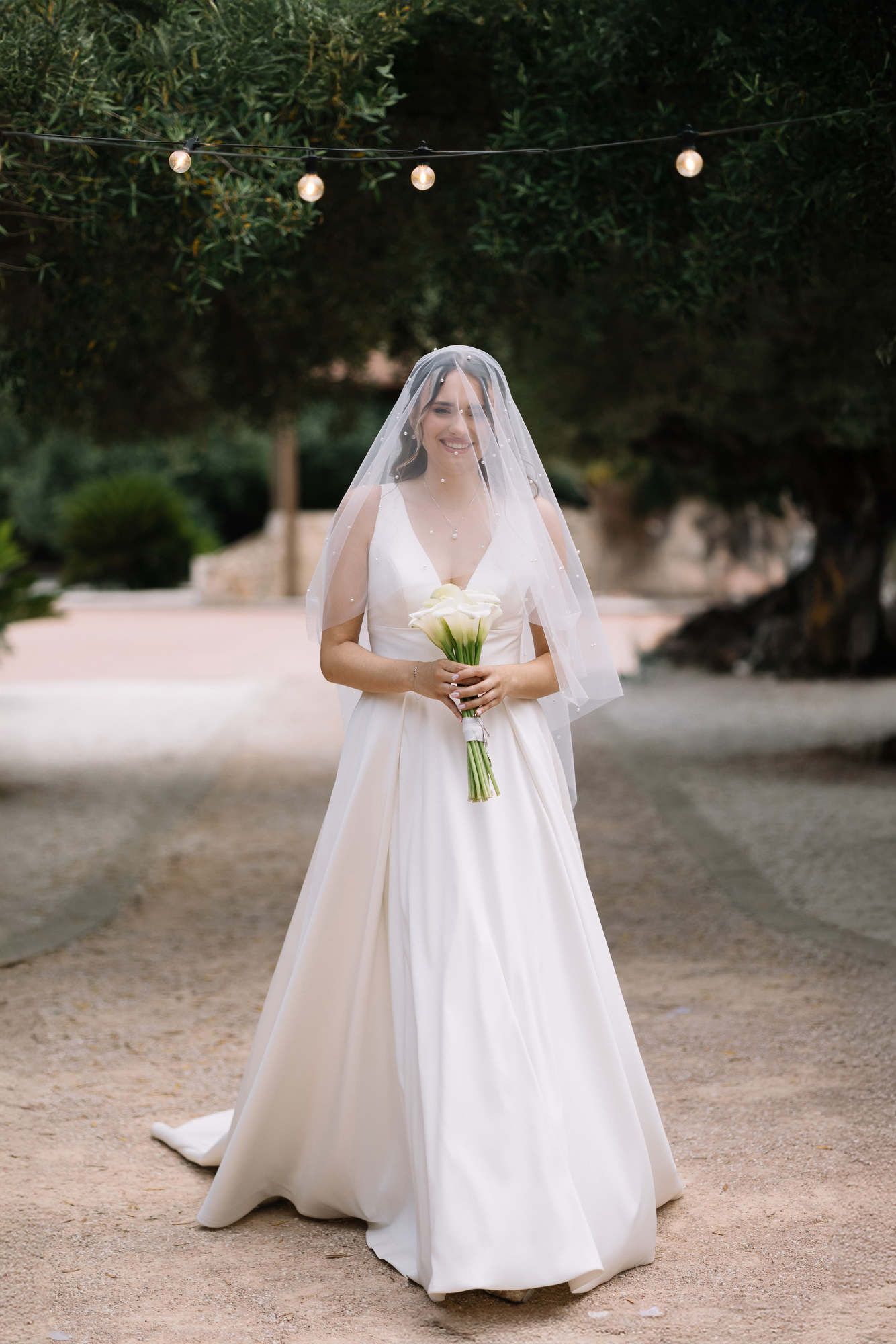 Bride walking to the wedding ceremony with a veil covering her face at Alqueria del Xúquer, featuring professional bridal makeup.