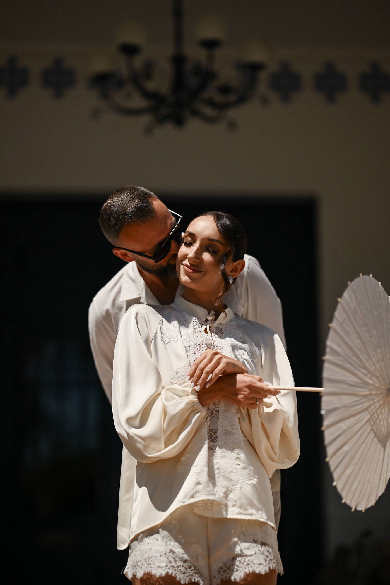 Groom hugs the bride in her morning robe with a sun parasol before she puts on her dress for the Villa Paula wedding ceremony.